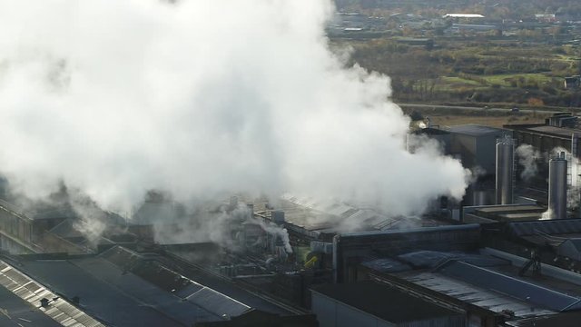Aerial view of thick steam being blown from a paper mill in the UK. Victorian architecture dominating over houses.