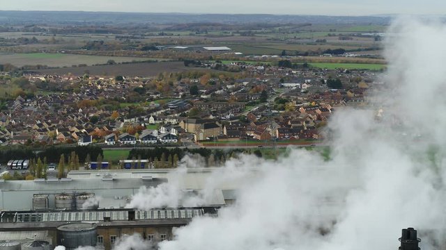 Static aerial conceptual shot of steam billowing from a factory in the UK which is dominating over neighboring housing.