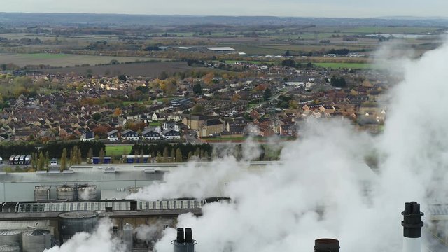 Aerial view of a factory in the UK blowing steam, dominating over houses.
