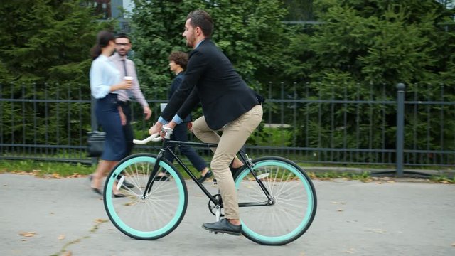 Handsome manager active young person is riding bike to office building in the morning wearing suit. Eco transport, modern city and healthy people concept.