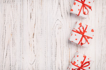 Valentine or other holiday handmade present in paper with red hearts and gifts box in holiday wrapper. Present box of gift on white wooden table top view with copy space, empty space for design
