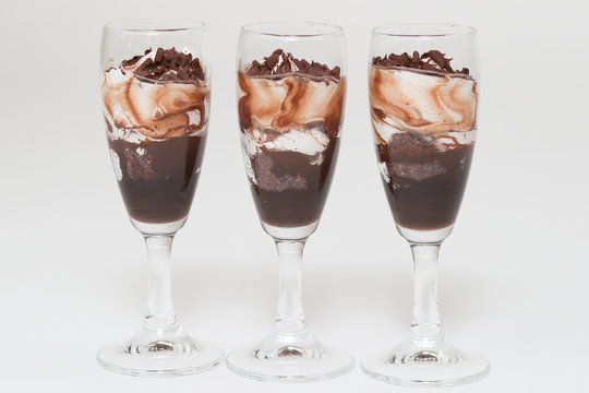Layered trifle dessert with chocolate sponge cake, whipped cream and fruit jelly in serving glasses. - Image
