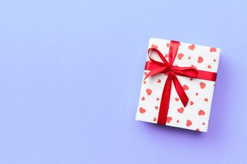 Gift box with red ribbon and heart on purple background, top view with copy space for text