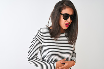 Chinese woman wearing striped t-shirt and sunglasses standing over isolated white background with hand on stomach because indigestion, painful illness feeling unwell. Ache concept.