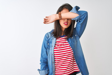 Young chinese woman wearing striped t-shirt and denim shirt over isolated white background covering eyes with arm, looking serious and sad. Sightless, hiding and rejection concept