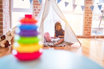 Beautiful toddler girl sitting on the floor playing with unicorn inside tipi at kindergarten © Krakenimages.com