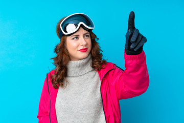 Skier woman with snowboarding glasses over isolated blue wall touching on transparent screen