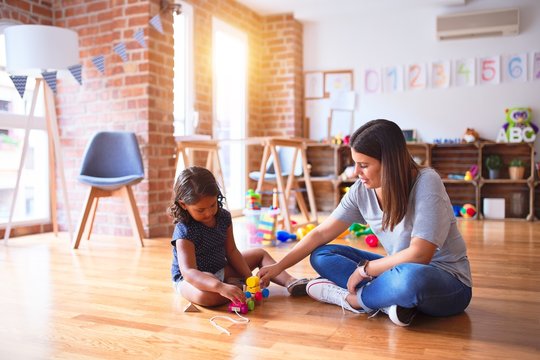 Beautiful teacher and toddler girl playing with train at kindergarten