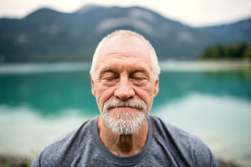 A front view portrait of senior man pensioner standing outdoors in nature.