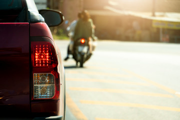 The back of a red pick-up truck stop and open brake light on the road with blurred of motorcycle.