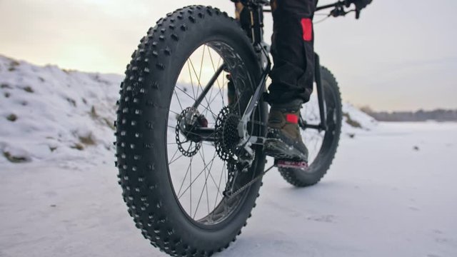 Professional extreme sportsman biker riding fat bike in outdoors. Close-up view of rear wheel. Cyclist ride in winter forest. Man on mountain bicycle with big tire. Snow fly into the lens camera.