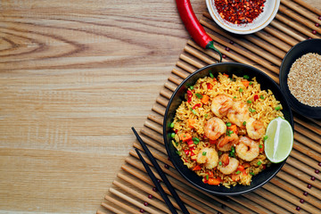 Traditional shrimps stir fried with eggs, vegetables and rice in a black bowl on a bamboo placemat. Healthy Asian meal with sesame and lime. Top view, directly above shot with space for text.