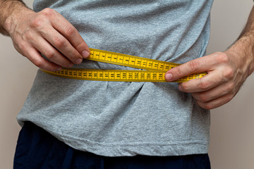 man in a gray T-shirt measures the waist with a yellow tape