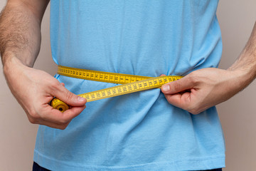 man in a blue T-shirt measures the waist with a yellow tape