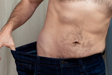Naklejka premium Slim man holding very big jeans. After a weight loss diet.