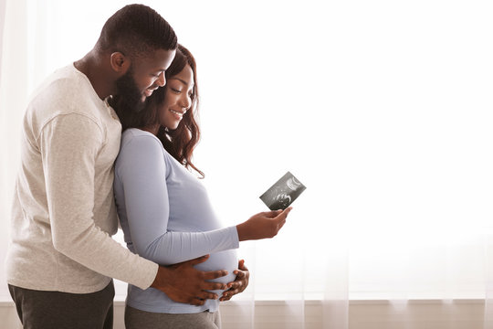 Emotional afro couple holding sonogram picture over white background