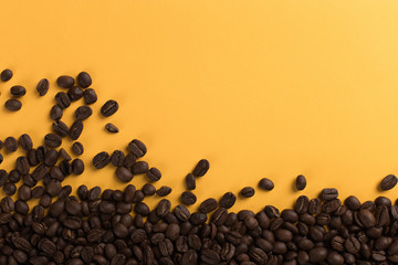 Coffee beans are scattered on a yellow paper background close-up, concept, commercial copy space.