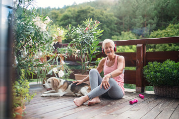 A senior woman with headphones outdoors on a terrace, resting after exercise.