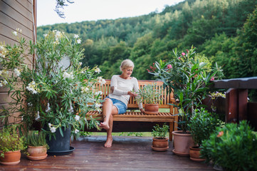 A senior woman sitting outdoors on a terrace in summer, resting.