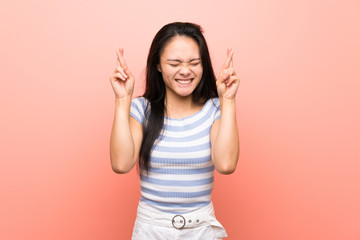 Teenager asian girl over isolated pink background with fingers crossing