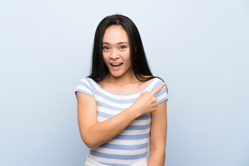 Fototapeta premium Teenager asian girl over isolated blue background pointing finger to the side