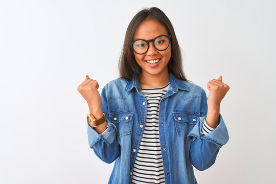 Young chinese woman wearing denim shirt and glasses over isolated white background celebrating surprised and amazed for success with arms raised and open eyes. Winner concept.