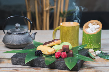 Sweet dessert, eclairs, raspberries and chocolate candies on a wooden table with decor in oriental, asian style.