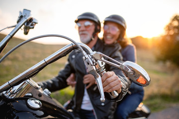 Cheerful senior couple travellers with motorbike in countryside.