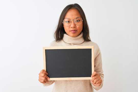 Young chinese woman wearing glasses holding blackboard over isolated white background with a confident expression on smart face thinking serious