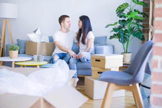 Young beautiful couple sitting on the sofa drinking coffee at new home around cardboard boxes