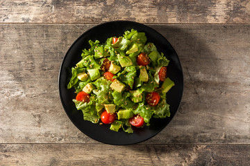 Salad with avocado, lettuce, tomato, seeds on wooden table. Top view