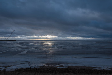 streams of light pour over the ice covered Gulf of Finland from a window formed in dramatic clouds