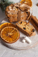 Traditional Italian biscotti or cantuccini cookies on a round white wooden board with cinnamon, dried orange slices and marshmallows on a light table near a Christmas tree. Christmas baking concept