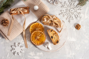 Traditional Italian biscotti or cantuccini cookies on a round white wooden board with cinnamon, dried orange slices and marshmallows on a light table near a Christmas tree. Christmas baking concept
