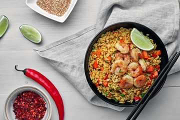 Traditional shrimps stir fried with eggs, vegetables and rice in a black bowl on a tablecloth. Healthy Asian meal with sesame and lime. Top view, directly above shot.