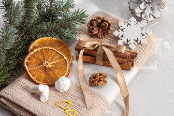 Cinnamon sticks are tied with a ribbon on a beige napkin with slices of dried orange, pine cone, nuts, snowflakes and marshmallows near a fir branch. Christmas concept.