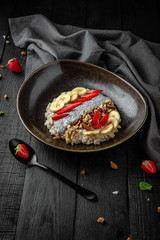 A healthy nutritious dietary breakfast made from a mixture of cereal flakes, chia seeds in yogurt, with banana, strawberries and nuts. Restaurant menu. Background black boards.