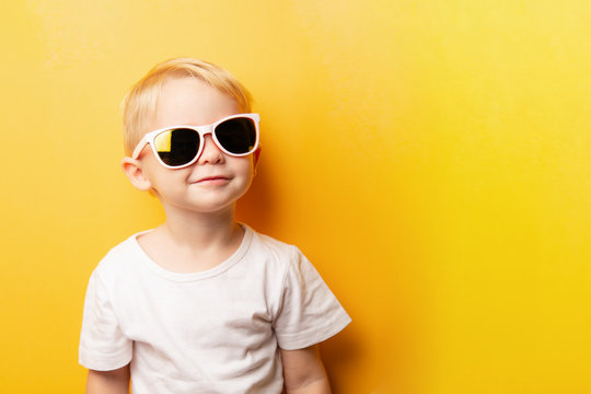 Portrait of cheerful smiling blond little boy in a white t-shirt on a yellow background. card with place for text