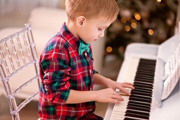 Boy in a checkered shirt and tie butterfly playing piano. Christmas concept.