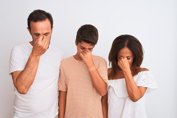 Family of three, mother, father and son standing over white isolated background tired rubbing nose and eyes feeling fatigue and headache. Stress and frustration concept.