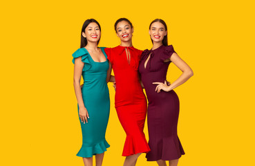 Fototapeta premium Three Multiracial Models In Dresses Standing Over Yellow Studio Background