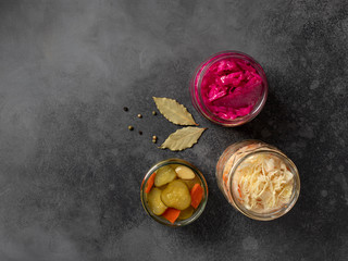 assortment of fermented vegetables: cabbage, cucumbers, carrots, in glass jars. dark concrete background, top view, copy space