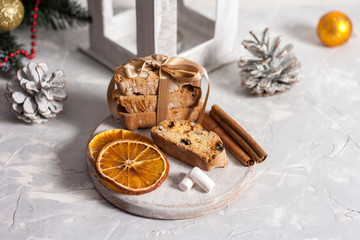 Traditional Italian biscotti or cantuccini cookies on a round white wooden board with cinnamon, dried orange slices and marshmallows on a light table near a Christmas tree. Christmas baking concept