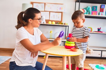 Beautiful teacher and toddler boy building pyramid with hoops bolcks at kindergarten