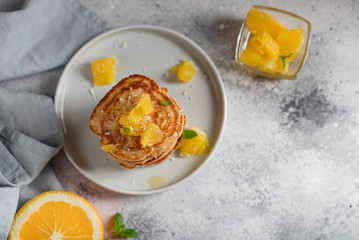 stack of homemade pancakes with orange and mint. healthy breakfast. gray concrete background, horizontal image, copy space