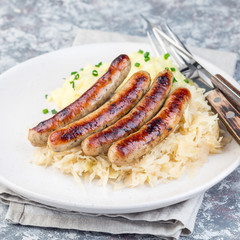 Roasted nuremberg sausages served with sour cabbage and mashed potatoes, on a white plate, square