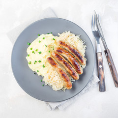 Roasted nuremberg sausages served with sour cabbage and mashed potatoes, on a gray plate, top view, square format