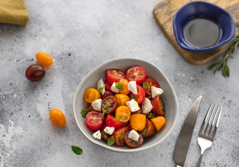salad with colorful cherry tomatoes, feta cheese, herbs, olive oil. Mediterranean food. gray concrete background, horizontal image, top view