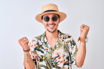 Young handsome man wearing Hawaiian shirt and summer hat over isolated background celebrating surprised and amazed for success with arms raised and open eyes. Winner concept.