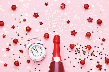 Flat lay of Christmas Celebration. Champagne bottle and alarm clock with Christmas decoration on pink background..